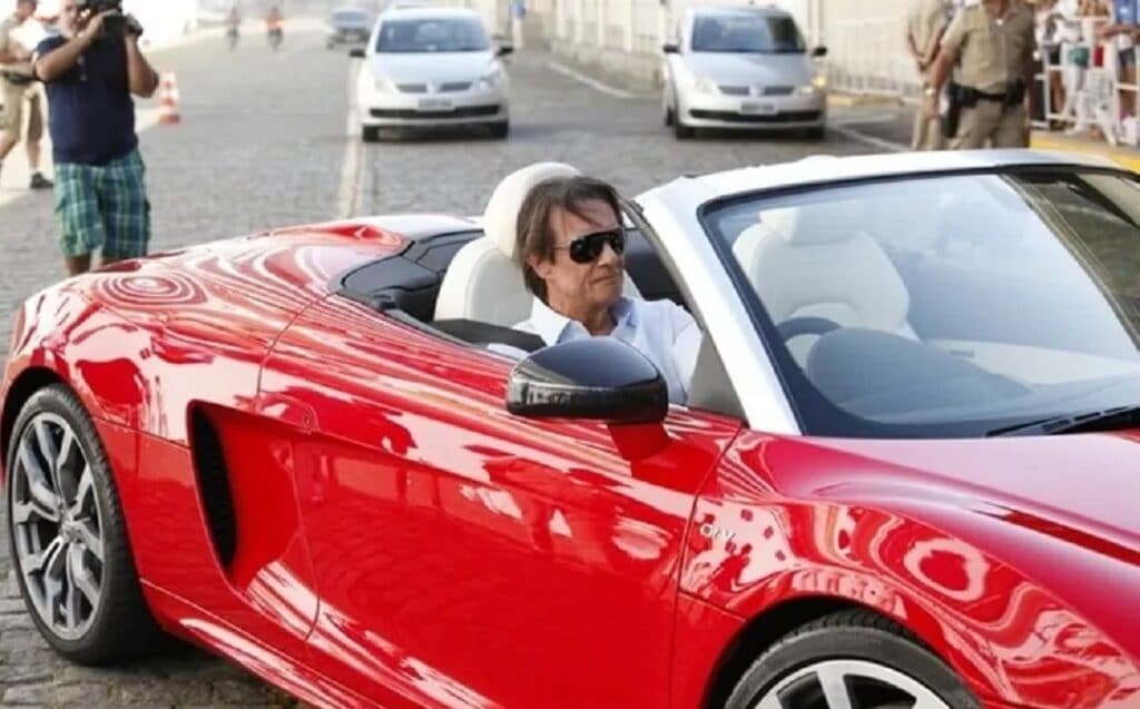 Imagem com foto do cantor Roberto Carlos dirigindo seu carro vermelho