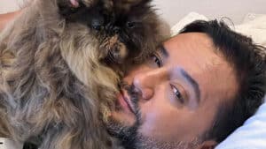Imagem com foto do apresentador Geraldo Luís deitado em uma cama com uma gatinha de estimação