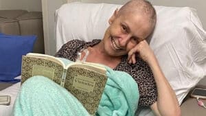 Imagem com foto de Susana Naspolini deitada em leito de hospital segurando um livro