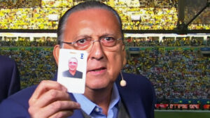 Imagem com foto de Galvão Bueno segurando seu crachá da Globo em uma cabine de transmissão em um estádio de futebol