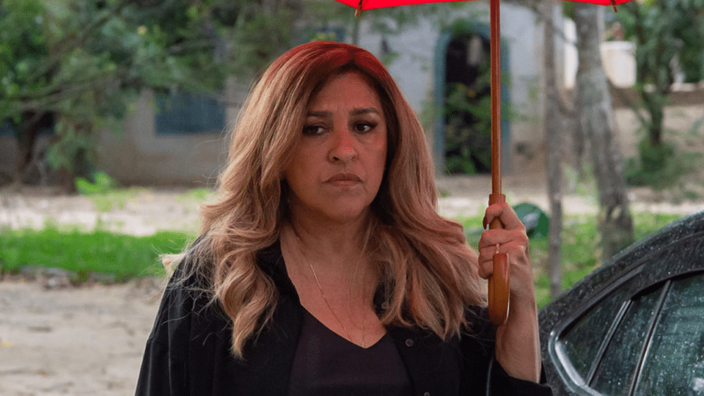Imagem com foto da atriz Regina Casé como Zoé segurando um guarda-chuva em cena de Todas as Flores