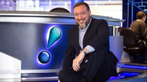 Imagem com foto do jornalista Franz Vacek sentado ao lado da bancada do RedeTV! News