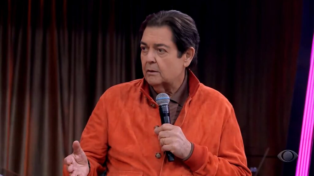 Foto do apresentador Faustão, usando uma jaqueta laranja, em seu programa na Band