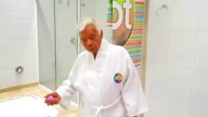 Imagem com foto de Gonçalo Roque, funcionário de Silvio Santos, no banheiro de casa vestindo um roupão com logo do SBT