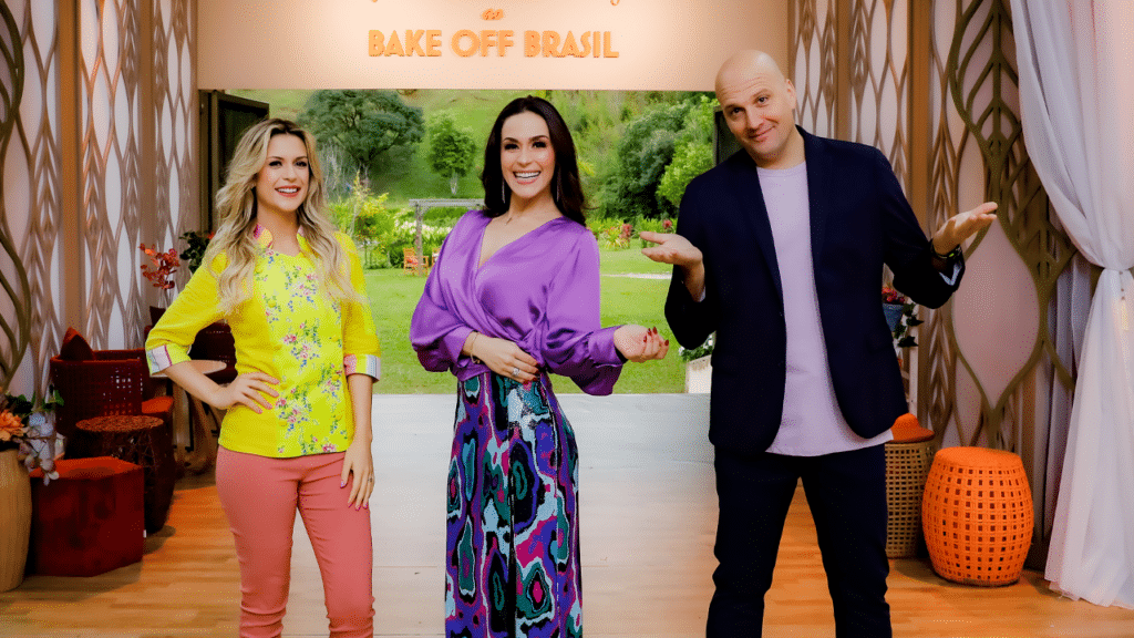 Imagem com foto de Beca Milano, Nadja Haddad e Giuseppe Gerundino no cenário do Bake Off Brasil