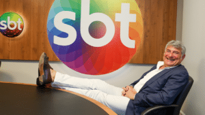 Cléber Machado sentado em uma cadeira e com os pés na mesa em uma sala de reunião executiva do SBT