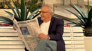 Carlos Alberto de Nóbrega sentado no banco de A Praça é Nossa com jornal nas mãos