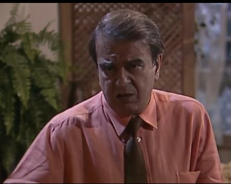 Na imagem, vemos o personagem Modesto Pires, da novela Tieta (1989), interpretado por Armando Bógus. Ele aparece com uma expressão séria e preocupada, com as sobrancelhas franzidas e a boca ligeiramente aberta, sugerindo um momento de tensão ou indignação