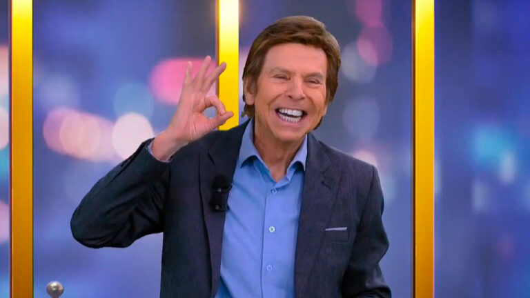 Nelson Rubens sorrindo no estúdio do TV Fama com microfone na lapela e fazendo gesto de OK com a mão