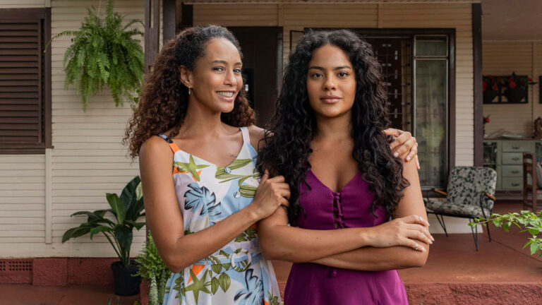 Taís Araujo como Raquel e Bella Campos como Fátima no remake de Vale Tudo, em frente a uma casa com varanda