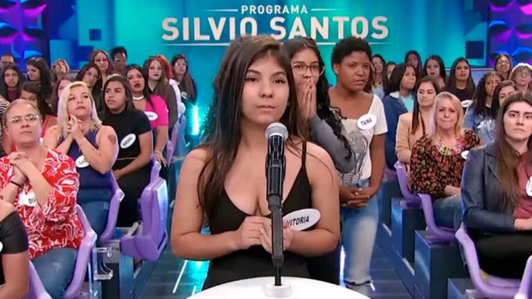 Vitória Regina em pé diante do microfone durante participação no Programa Silvio Santos com plateia ao fundo