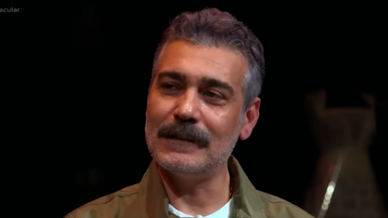 Caner Cindoruk durante entrevista com fundo escuro e vestindo jaqueta verde clara