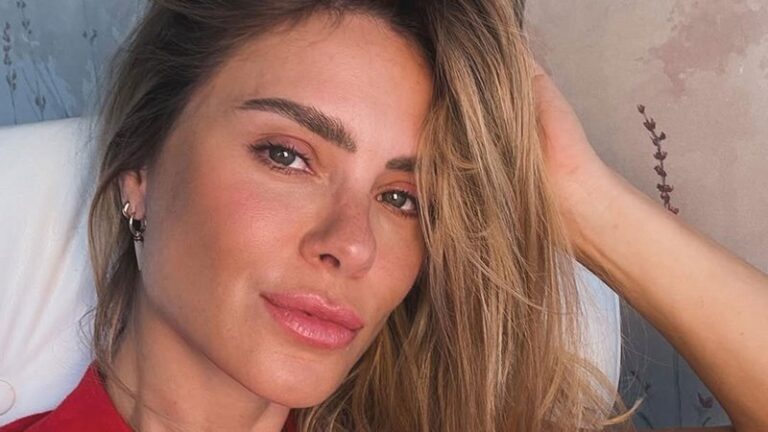 Carolina Dieckmann posa em um close natural, com expressão serena e olhar direto para a câmera. A atriz exibe maquiagem leve e batom rosado, com os cabelos soltos e levemente despenteados, apoiando uma das mãos na cabeça. A iluminação suave valoriza os traços da artista em um ambiente de fundo neutro e delicado.