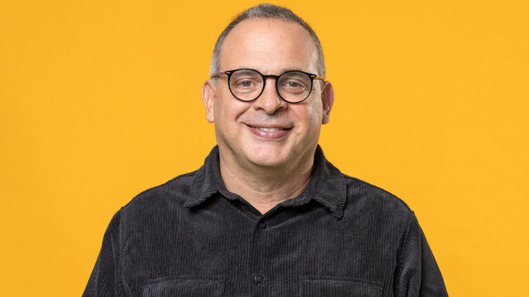 Fabrício Mamberti posando para foto com camisa preta em fundo amarelo