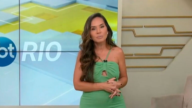Isabele Benito apresenta o SBT Rio em frente ao telão com o logotipo do telejornal exibido no estúdio da emissora