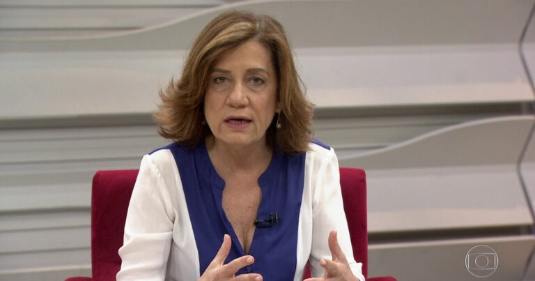 A jornalista Míriam Leitão aparece em estúdio da TV Globo durante participação em um programa da GloboNews. Sentada em uma poltrona vermelha, ela usa uma blusa branca com detalhes em azul e gesticula com as mãos enquanto analisa o cenário político e econômico. Com expressão séria, Míriam mantém seu tom característico de comentarista experiente.