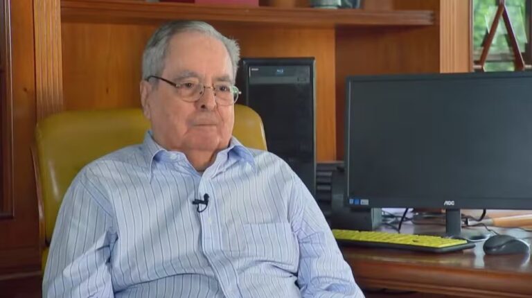 Benedito Ruy Barbosa sentado em cadeira na frente de um computador, com expressão séria