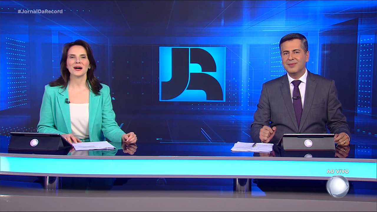 Foto de Giovanna Risardo e Clébio Cavagnolle na bancada do Jornal da Record