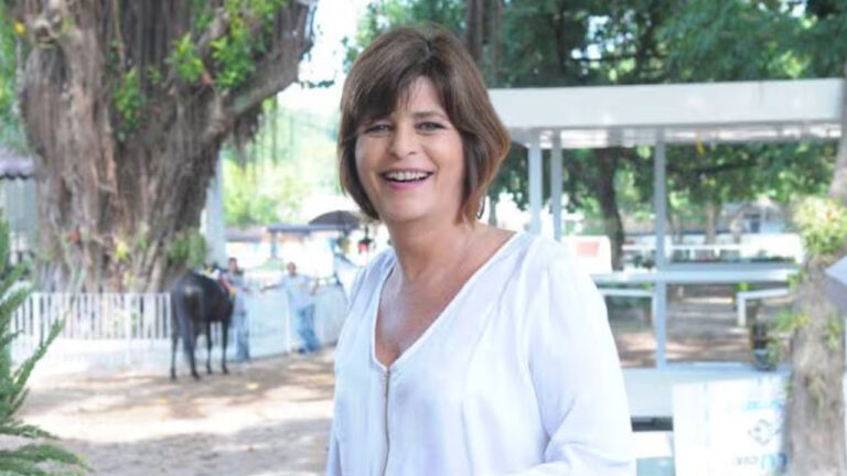 Cristianne Fridman sorrindo em local aberto com árvores e estrutura de haras ao fundo