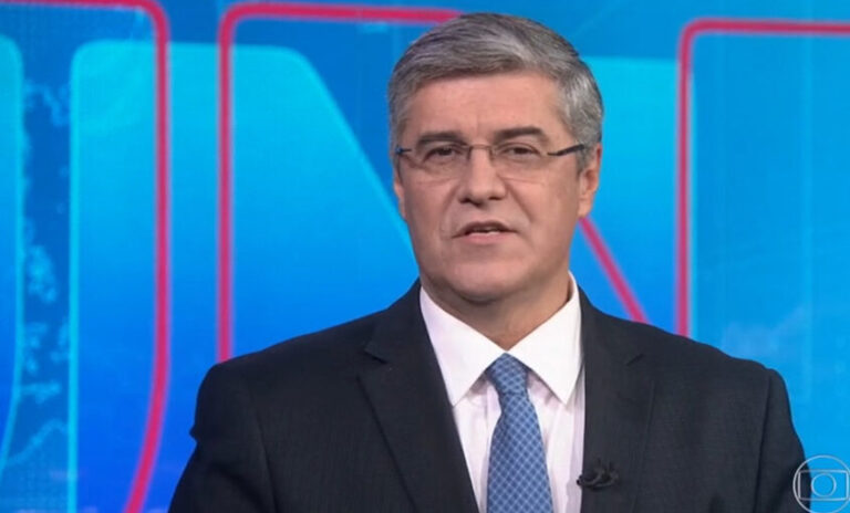 Flávio Fachel com um terno e o fundo do Jornal Nacional