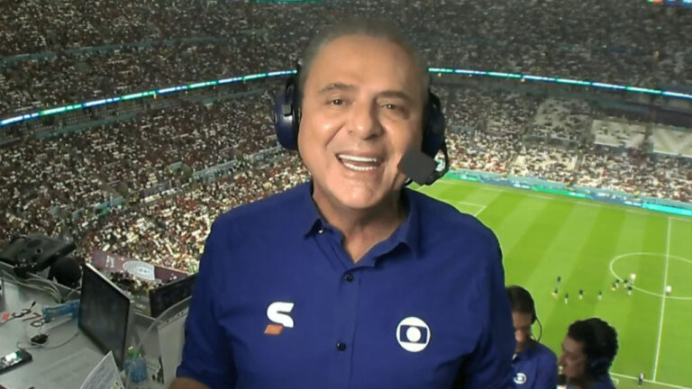 Luis Roberto com fone de ouvido e microfone na cabine de transmissão da Globo durante jogo em estádio lotado