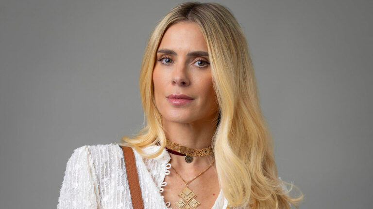 Carolina Dieckmmann com cabelo solto e blusa branca em ensaio promocional com fundo cinza neutro