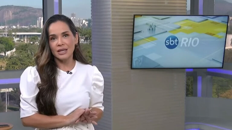 Isabele Benito apresentando o SBT Rio em estúdio com telão e paisagem urbana ao fundo