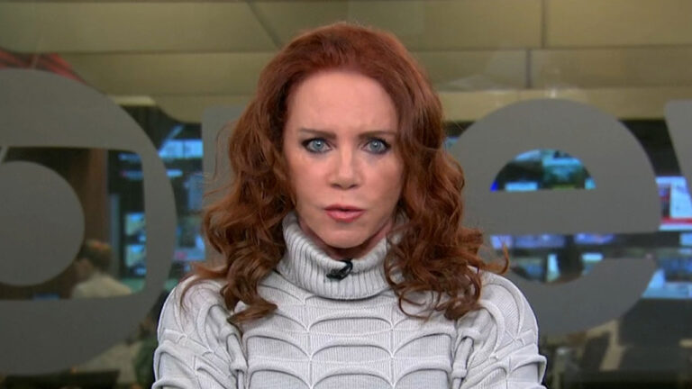 Leilane Neubarth com suéter claro e cabelo ruivo solto durante apresentação do Conexão GloboNews no estúdio da emissora