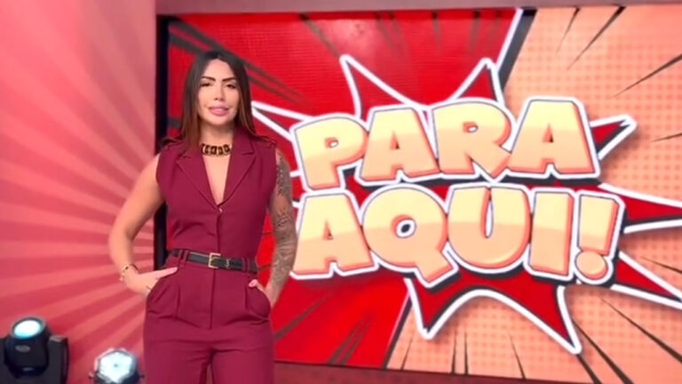 Babi Montello em pé no estúdio do programa Para Aqui! da RedeTV! diante do telão com o logo da atração