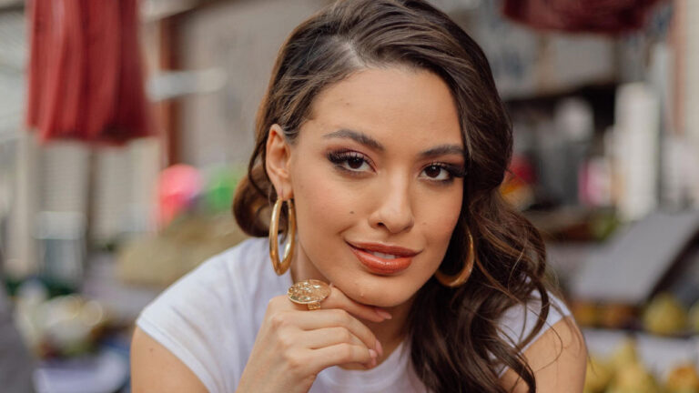 Beatriz Reis conhecida como Bia do Brás com cabelo castanho solto brincos de argola dourados e anel apoiando o queixo