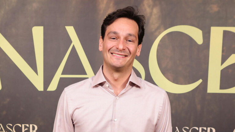 Bruno Luperi sorrindo com camisa social clara durante evento de lançamento da novela Renascer diante de painel com o título