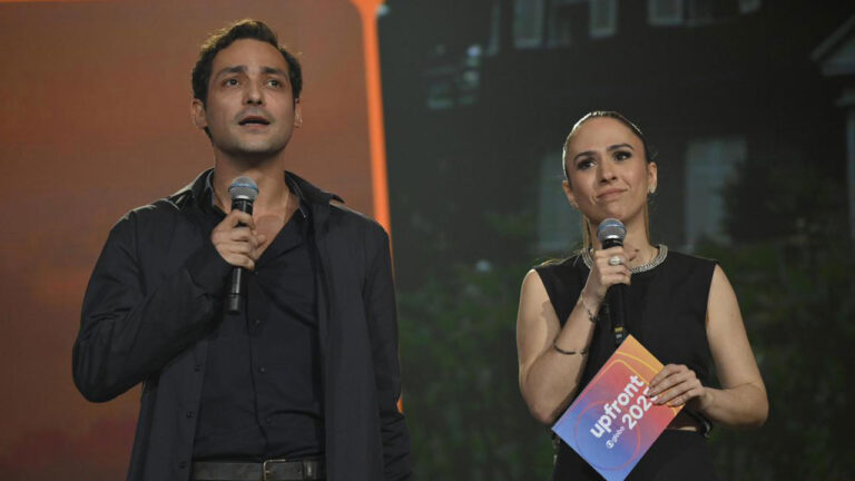 Eduardo Sterblitch e Tatá Werneck no palco com microfones durante evento Upfront Globo 2025, ela segurando ficha colorida