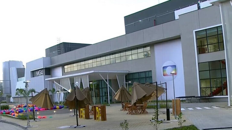 Prédio do complexo MG4 da Globo com logotipo da emissora na fachada e área externa com mesas e guarda-sóis