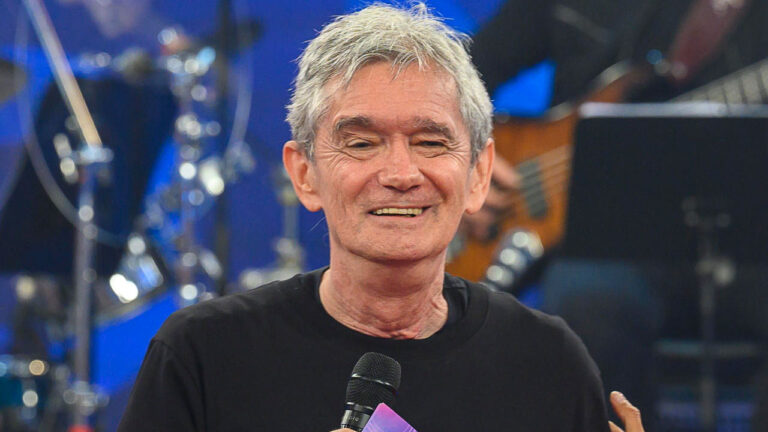 Serginho Groisman sorrindo e segurando microfone durante o Altas Horas com banda ao fundo