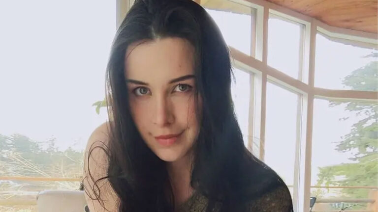 Aella influenciadora norte-americana com cabelo solto escuro posa em ambiente iluminado por janelas grandes de vidro