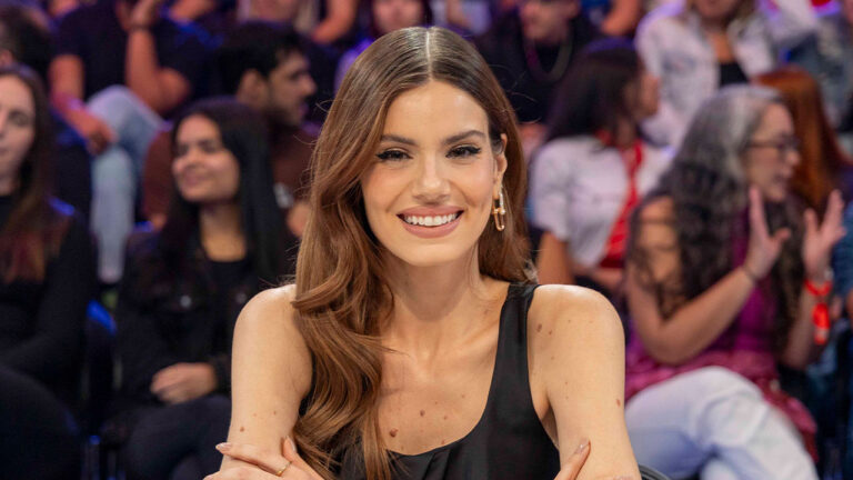 Camila Queiroz sorrindo de vestido preto no Domingão com Huck sentada em frente à plateia do programa