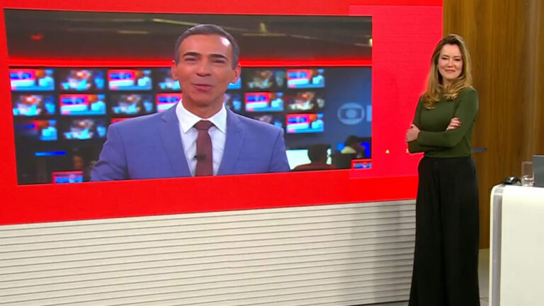 César Tralli aparece em telão de redação enquanto Natuza Nery sorri ao lado no estúdio do Edição das 18h da GloboNews