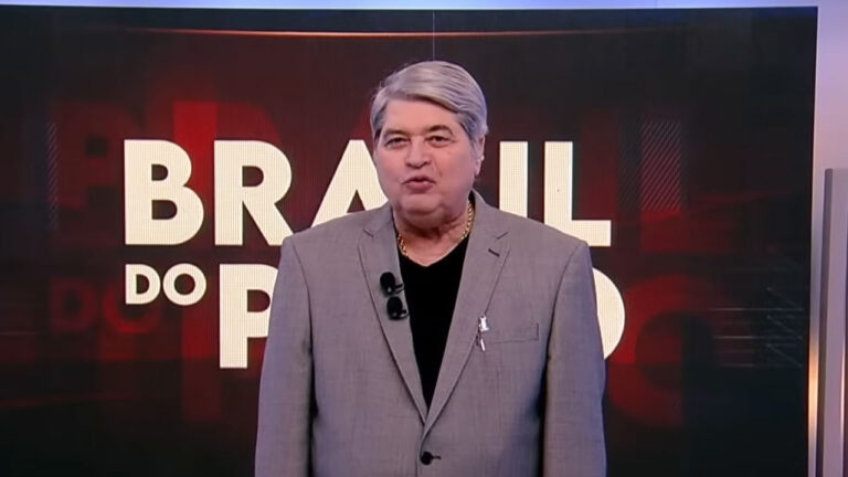 Datena de terno cinza apresenta o programa Brasil do Povo da RedeTV! diante de telão com o nome da atração