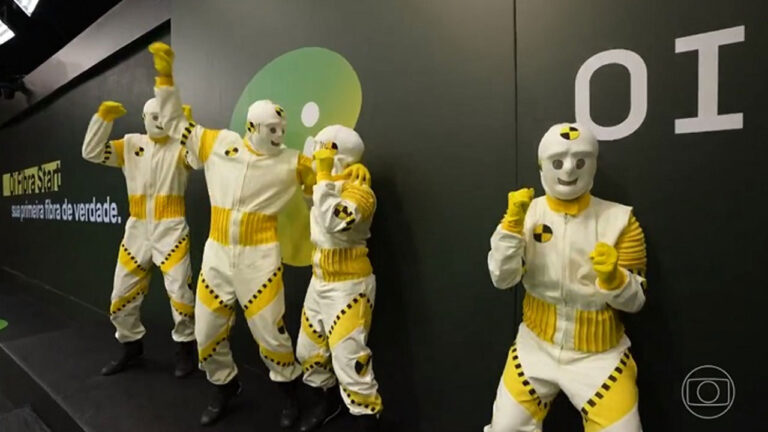 Dummys vestidos de branco e amarelo participam de ação comercial da Oi no BBB 24 em frente a painel com logotipo da marca