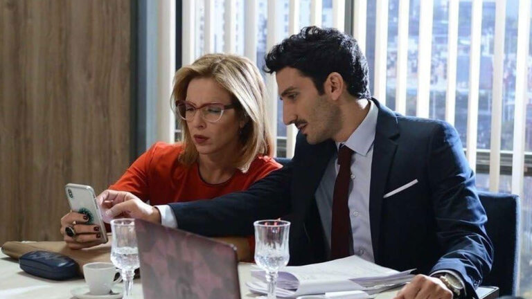 Laura (Carla Peterson) mostra celular para Gastão (Juan Minujín) em cena de escritório na novela 100 días para Enamorarse