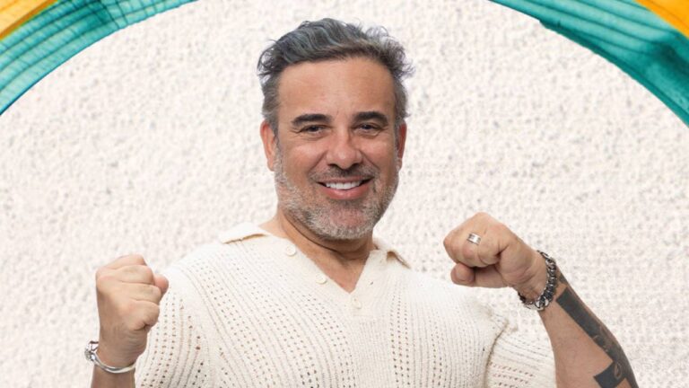 Fabiano Morais com cabelo grisalho e suéter de tricô sorrindo e levantando os punhos em gesto de vitória