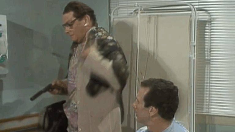 Ismael disfarçado com peruca e roupas femininas segura arma enquanto conversa com homem sentado em cama de hospital em cena da novela A Viagem da TV Globo