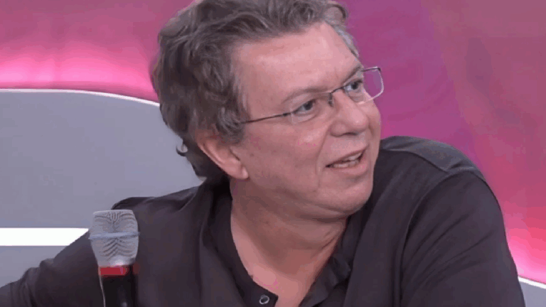 Boninho sentado em estúdio com microfone e fundo rosa iluminado