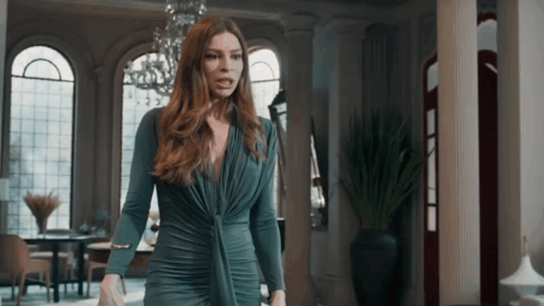 Mulher de vestido verde caminha com expressão preocupada em sala elegante em cena da novela Três Graças