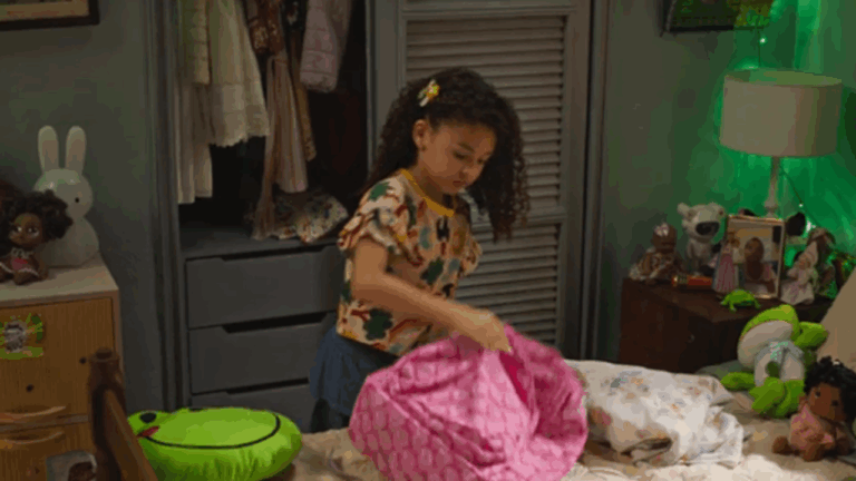 Cena da novela Dona de Mim, mostrando a personagem infantil Sofia em seu quarto, arrumando uma mochila cor-de-rosa sobre a cama, cercada por brinquedos e objetos coloridos