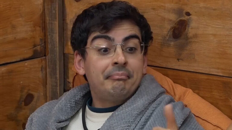 Dudu Camargo com óculos e robe cinza gesticula com o dedo e faz uma expressão de surpresa em cena do reality show A Fazenda 17