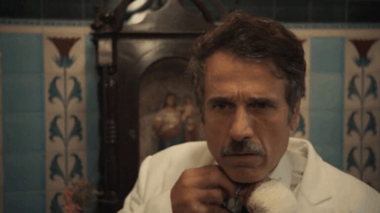 Ernesto ajusta a gravata com expressão séria em cena da novela Êta Mundo Melhor! da TV Globo