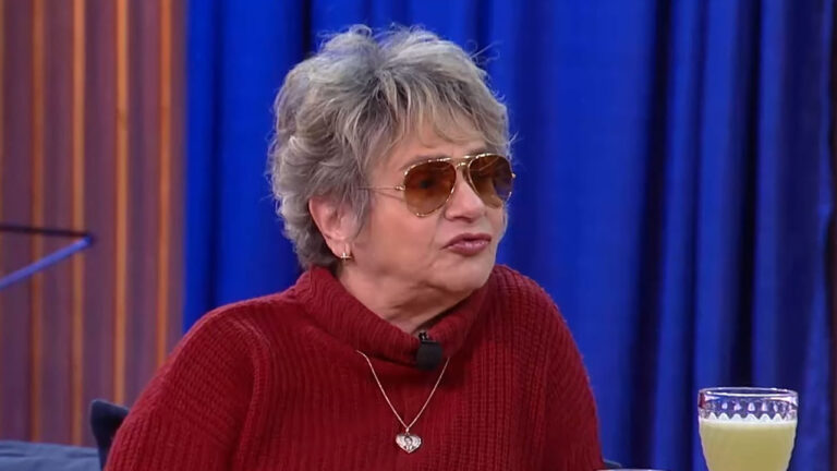 A atriz e comediante Fafy Siqueira com óculos de sol e suéter vermelho durante entrevista em programa com cenário de cortina azul