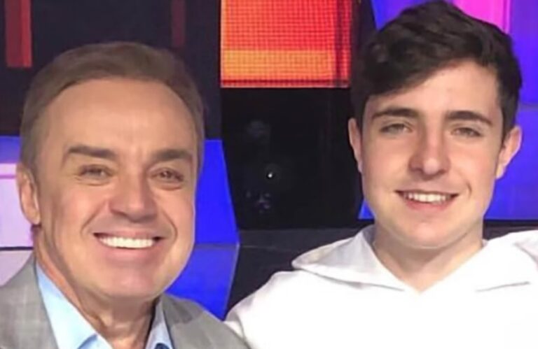 Gugu Liberato e João Augusto Liberato sorrindo juntos em estúdio com painel colorido ao fundo