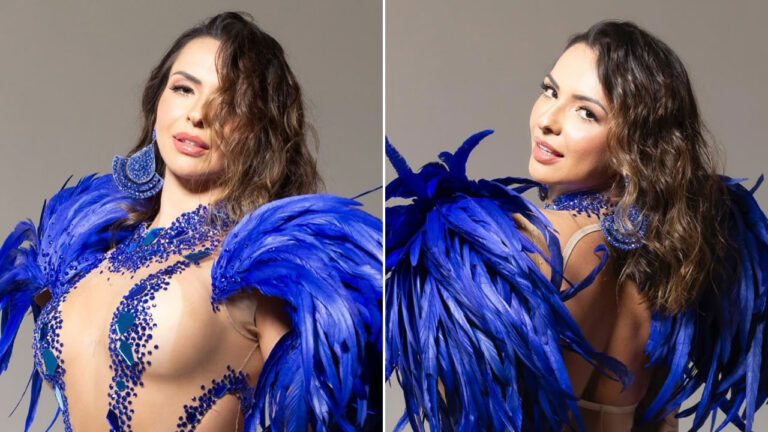 Karol Rosalin com fantasia azul de penas e pedras brilhantes, posando em estúdio com fundo claro para ensaio de Carnaval